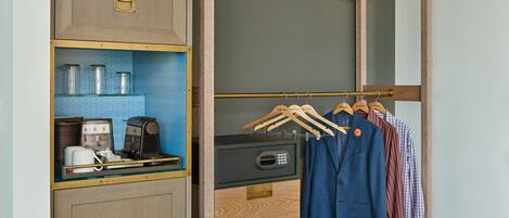 Ein begehbarer Kleiderschrank mit Holzschrank, Kaffeemaschine und Kleiderbügeln mit Kleidung.
