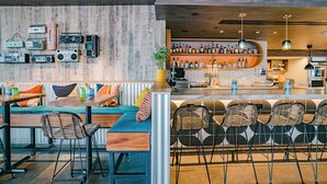 Un espace bar avec un mur en bois, des tabourets de bar et un coin salon comprenant un canapé et des fauteuils.