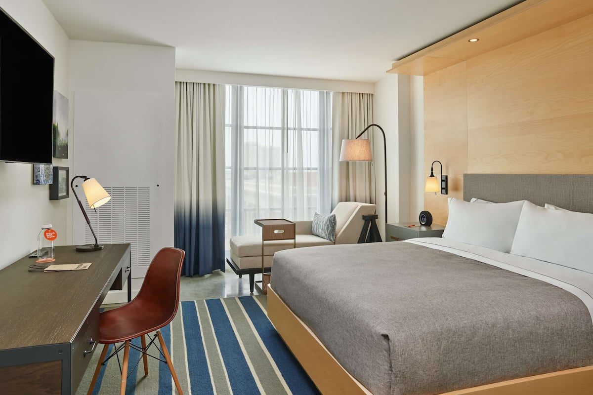 Une chambre d’hôtel avec un grand lit, un bureau avec une chaise, une télévision et une fenêtre avec des rideaux.