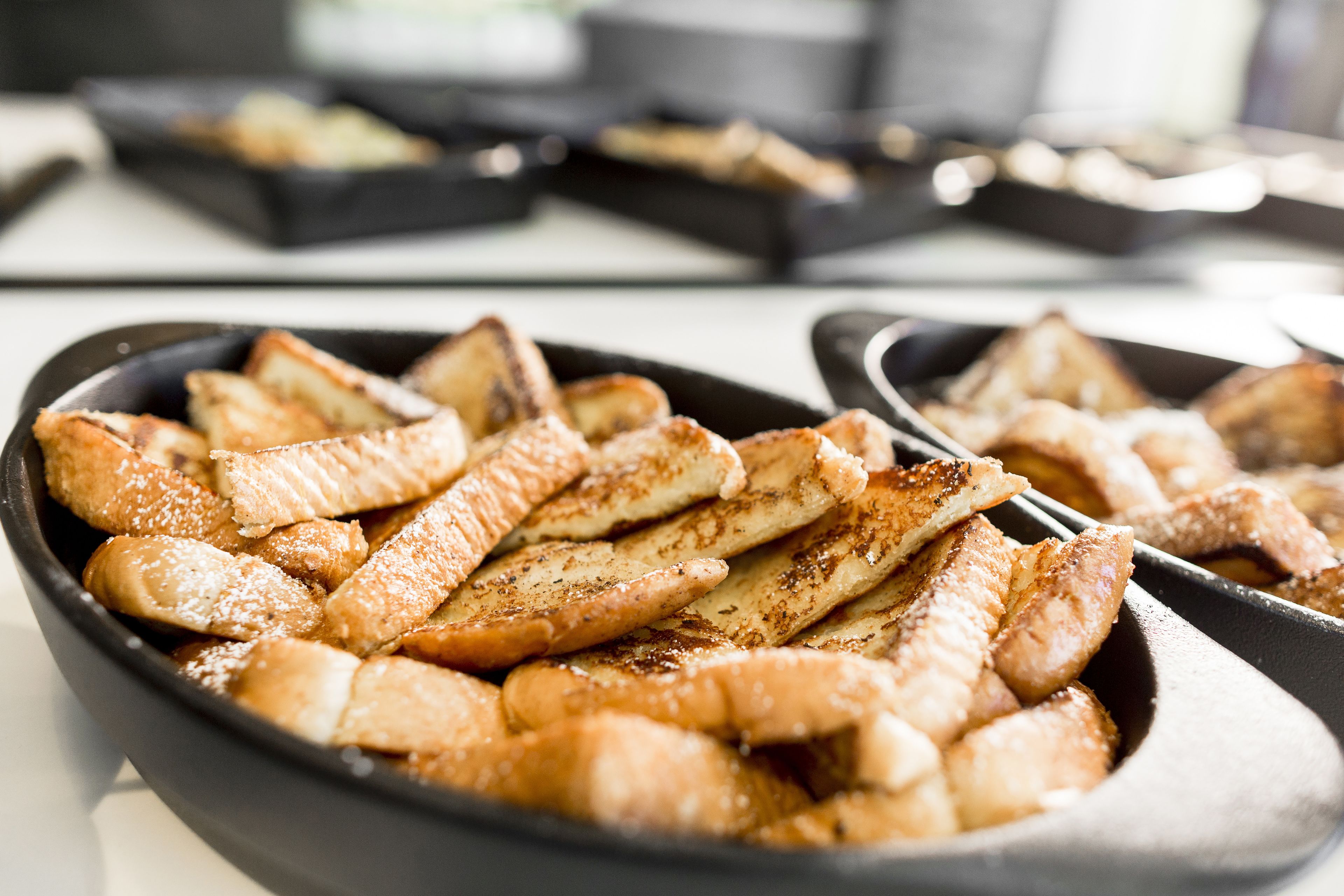 A close-up of a skillet filled with golden-brown pancakes, with a blurred background of similar cookware.