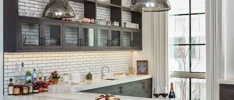 Une cuisine dotée d’un îlot en marbre, de meubles avec des portes en verre et de luminaires suspendus.