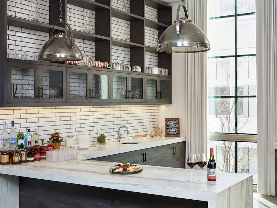 A kitchen with a marble island, glass cabinets, and hanging pendant lights.