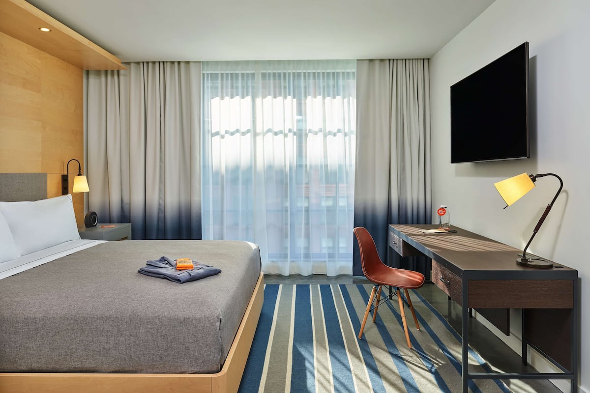 Une chambre d’hôtel avec un lit, un bureau, une chaise, une télévision et une fenêtre avec des rideaux.