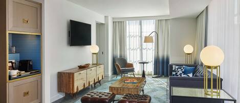A modern hotel room with a wooden cabinet, a flat-screen TV, a sofa, a coffee table, and a dining area.