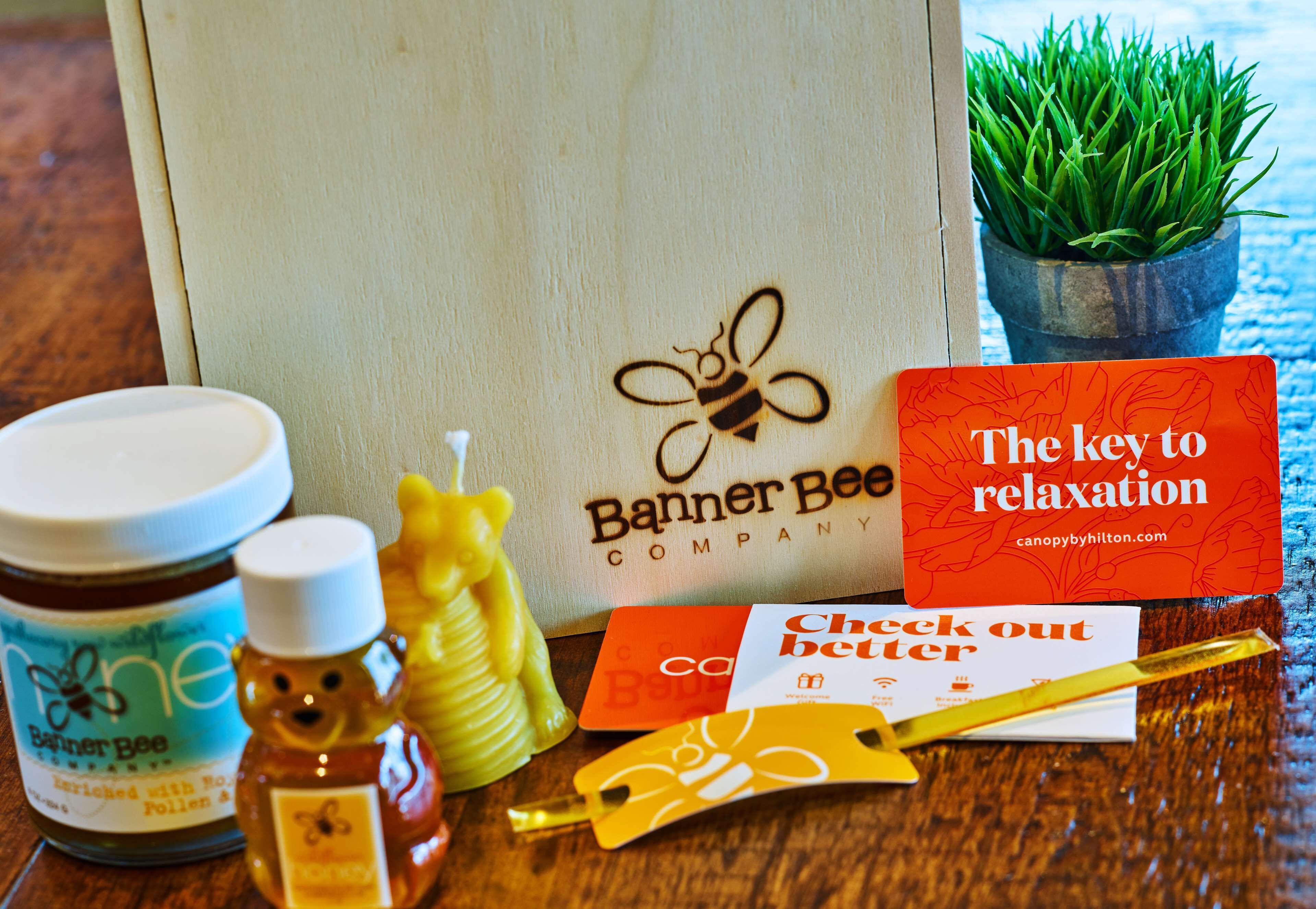 A wooden table with a honey jar, a honey dipper, a bee-shaped honey dipper, a card, a credit card, and a small potted plant.