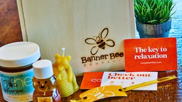 A wooden table with a honey jar, a honey dipper, a bee-shaped honey dipper, a card, a credit card, and a small potted plant.