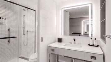 Un bany modern amb plat de dutxa envidriat, un lavabo blanc i un mirall gran amb il·luminació integrada.
