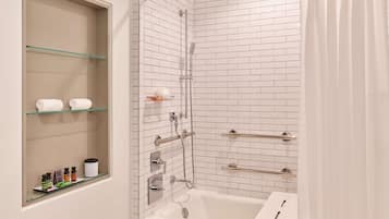 Un baño moderno con un estante de vidrio que contiene artículos de aseo, una bañera blanca y una zona de ducha con puerta de cristal.