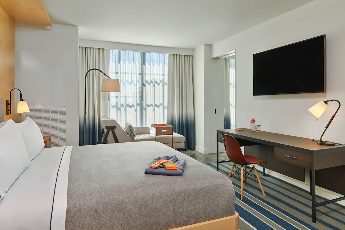 Une chambre d’hôtel avec un lit, un bureau, une chaise, une télévision et une fenêtre avec des rideaux.