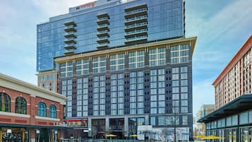 Hotel features a sleek glass facade, balconies, and a tranquil courtyard with seating areas and a fountain.