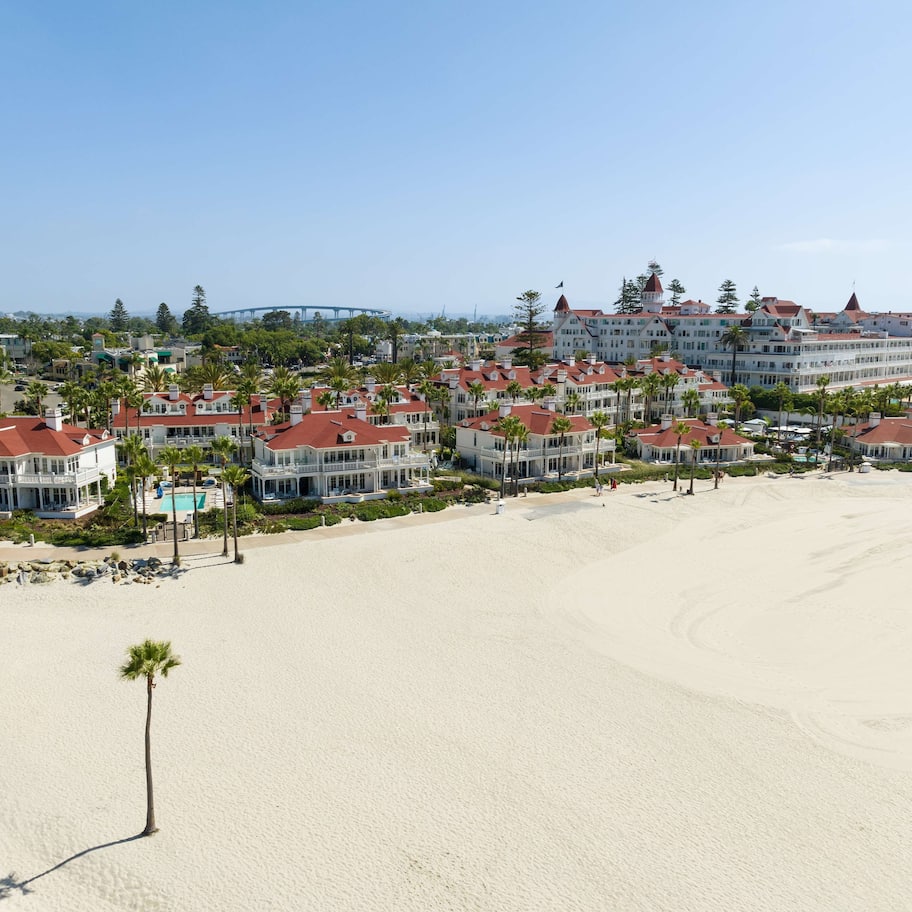 A beachfront hotel with multiple buildings, a sandy beach, and palm trees.