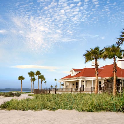 A beachfront property with a red-roofed house, palm trees, and a sandy beach.