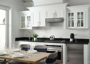 A modern kitchen with white cabinetry, a black countertop, and a dining area with wicker chairs.