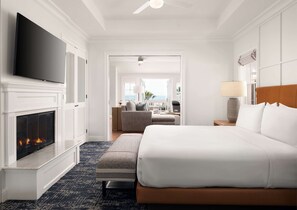 A hotel room with a fireplace, a large bed, a TV, and a view of the ocean.
