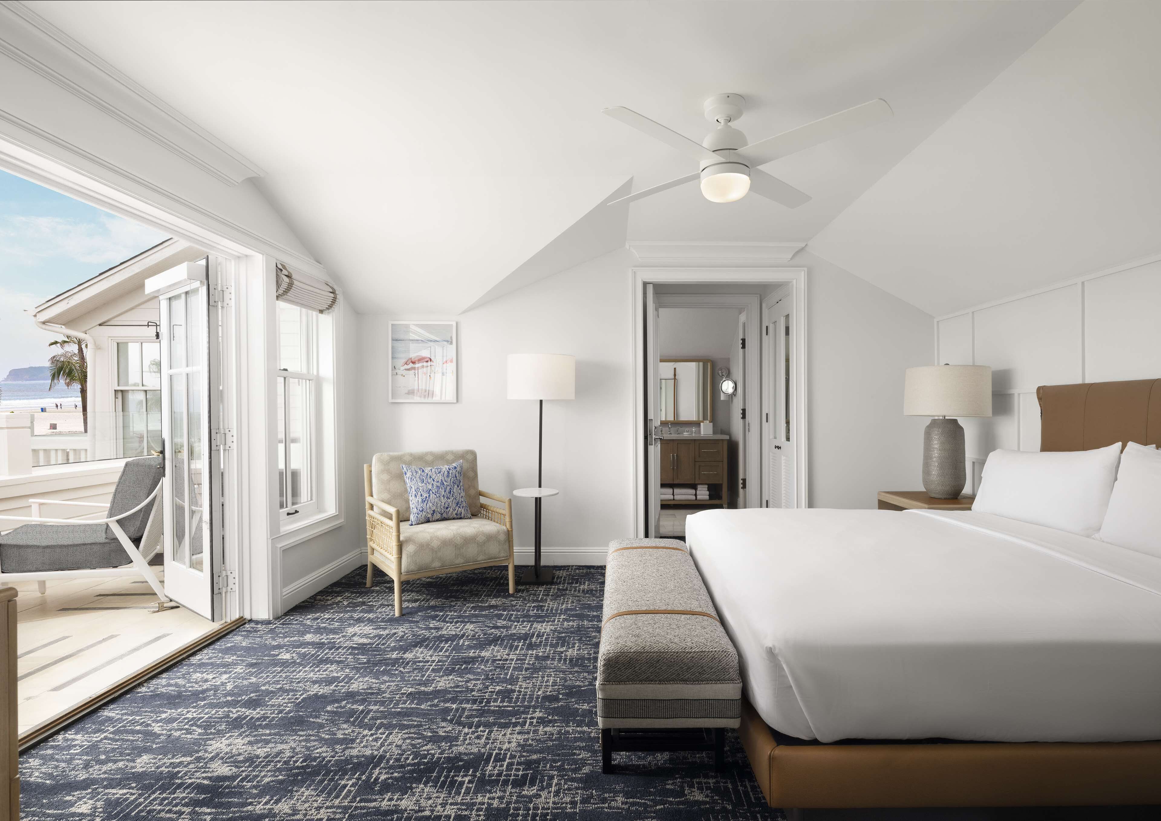 Ein Hotelzimmer mit einem großen Bett, einem Sessel, einem Schreibtisch, einer Lampe und einem Deckenventilator.