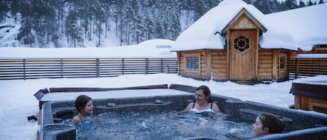 Una cabaña de madera con techo nevado y puerta de madera con un ventanal circular.