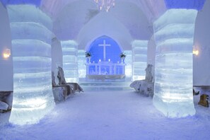 Interior de una iglesia de hielo con un altar central, bancos y velas.