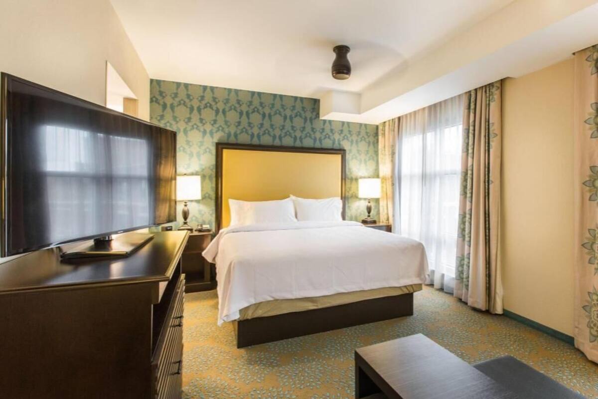 Une chambre d’hôtel avec un lit, des lampes de chevet, une télévision, un bureau et une grande fenêtre avec des rideaux.