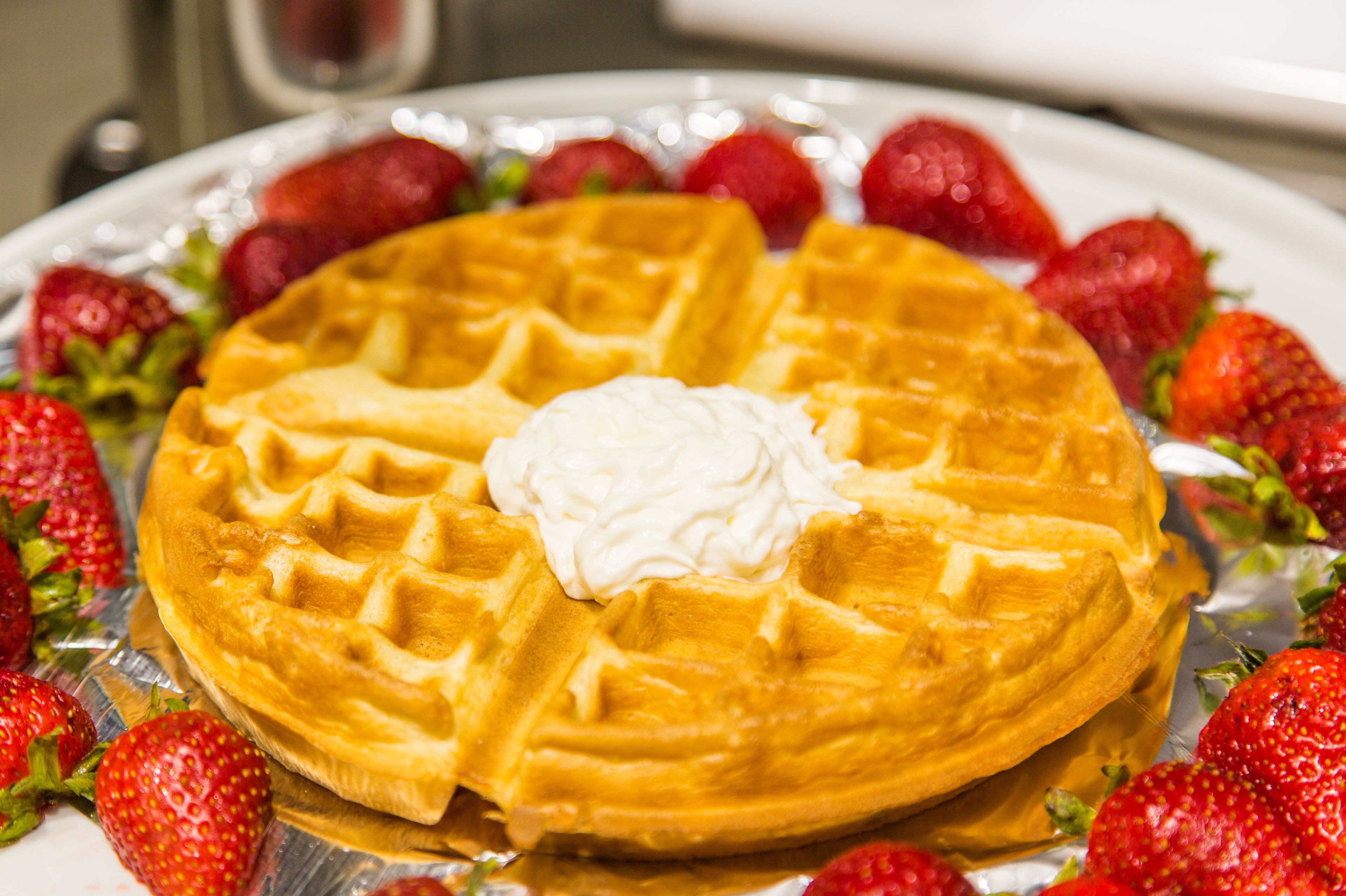 A waffle with whipped cream and strawberries on a plate.