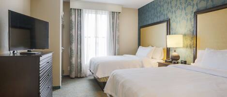 A hotel room with two beds, a TV, a dresser, and a window with curtains.