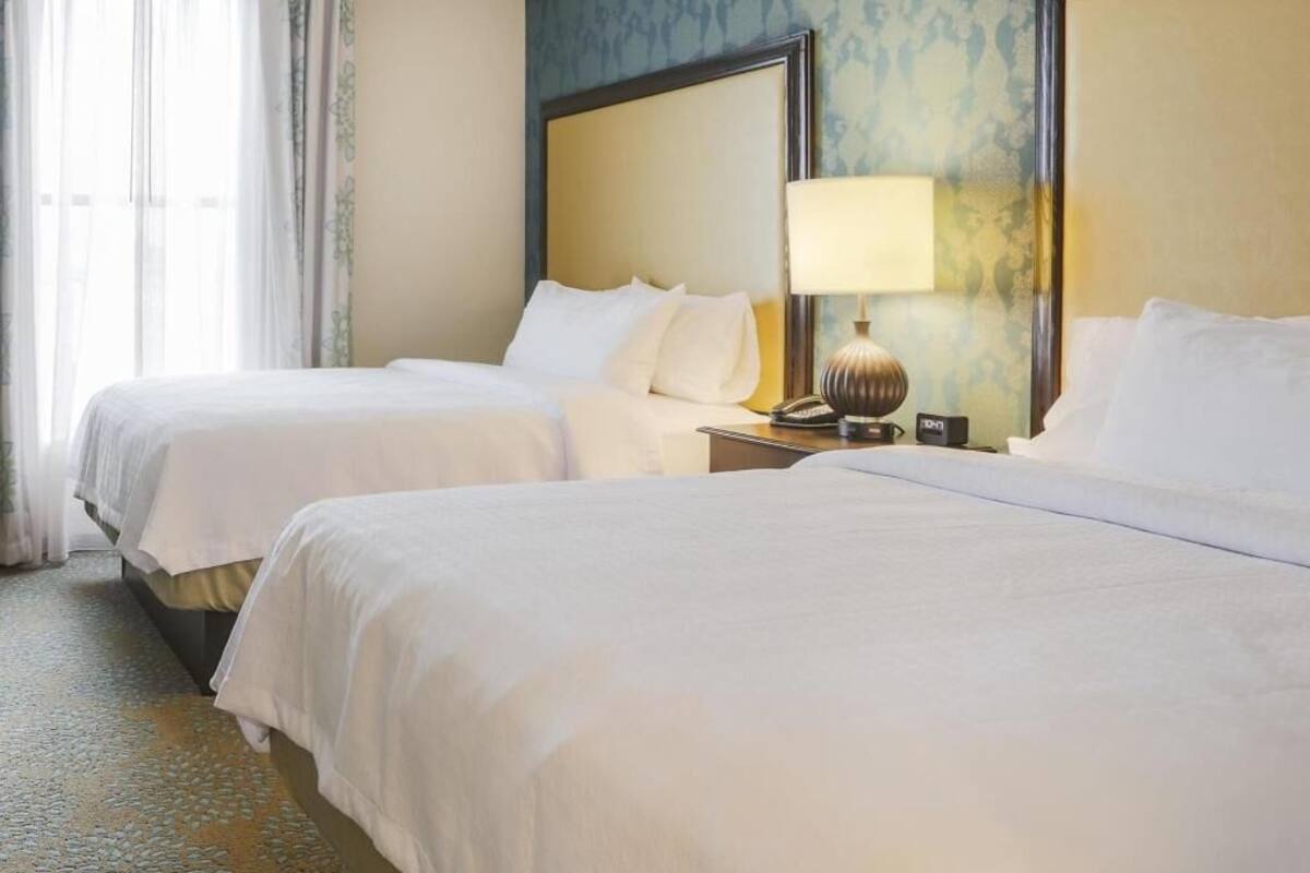 Une chambre d’hôtel avec deux lits, une table de chevet avec une lampe et une fenêtre avec des rideaux.