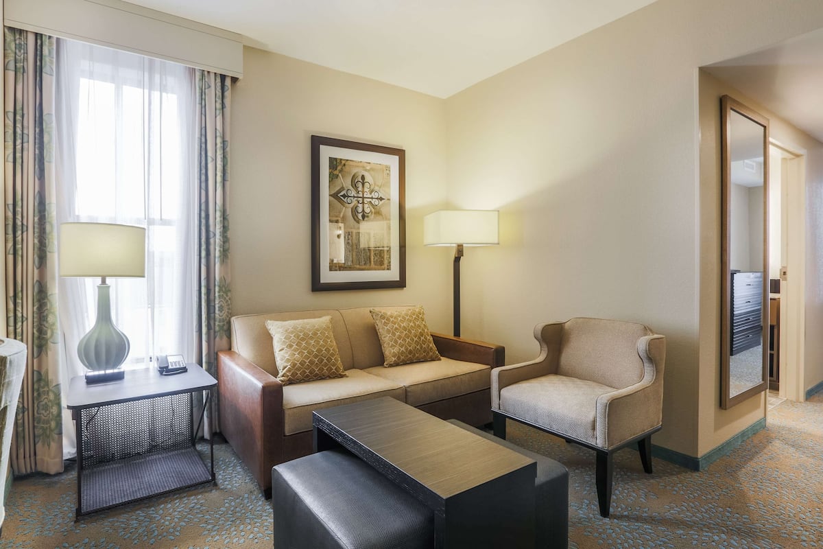Une chambre d’hôtel équipée d’un canapé, d’un fauteuil, d’une petite table, d’une lampe et d’une œuvre d’art encadrée au mur.
