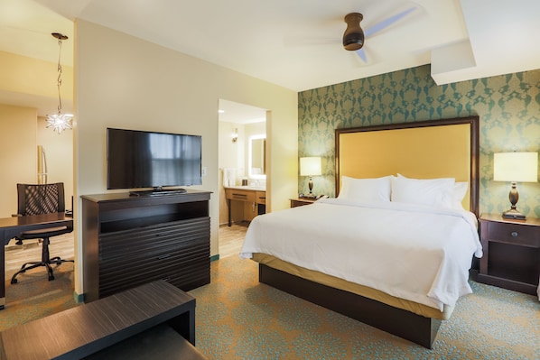 A hotel room with a large bed, a desk, a chair, a television, and a ceiling fan.