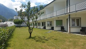 A building with a flat roof, a balcony with a metal railing, and a grassy courtyard with a tree. - Motel Des Sports (Martigny)