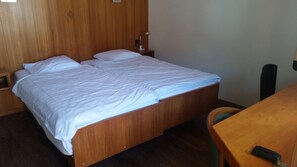 A single bed with a wooden frame and white bedding in a room with wooden walls and a small table. - Motel Des Sports (Martigny)