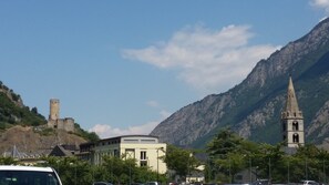 A town with a historic tower, a church with a tall spire, and a modern building in the foreground. - Motel Des Sports (Martigny)