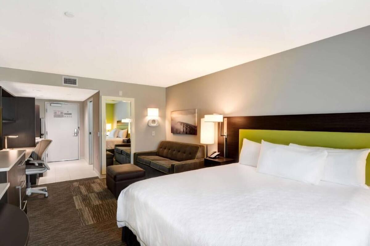 A hotel room with a bed, a desk, a chair, a sofa, a lamp, and a painting on the wall.