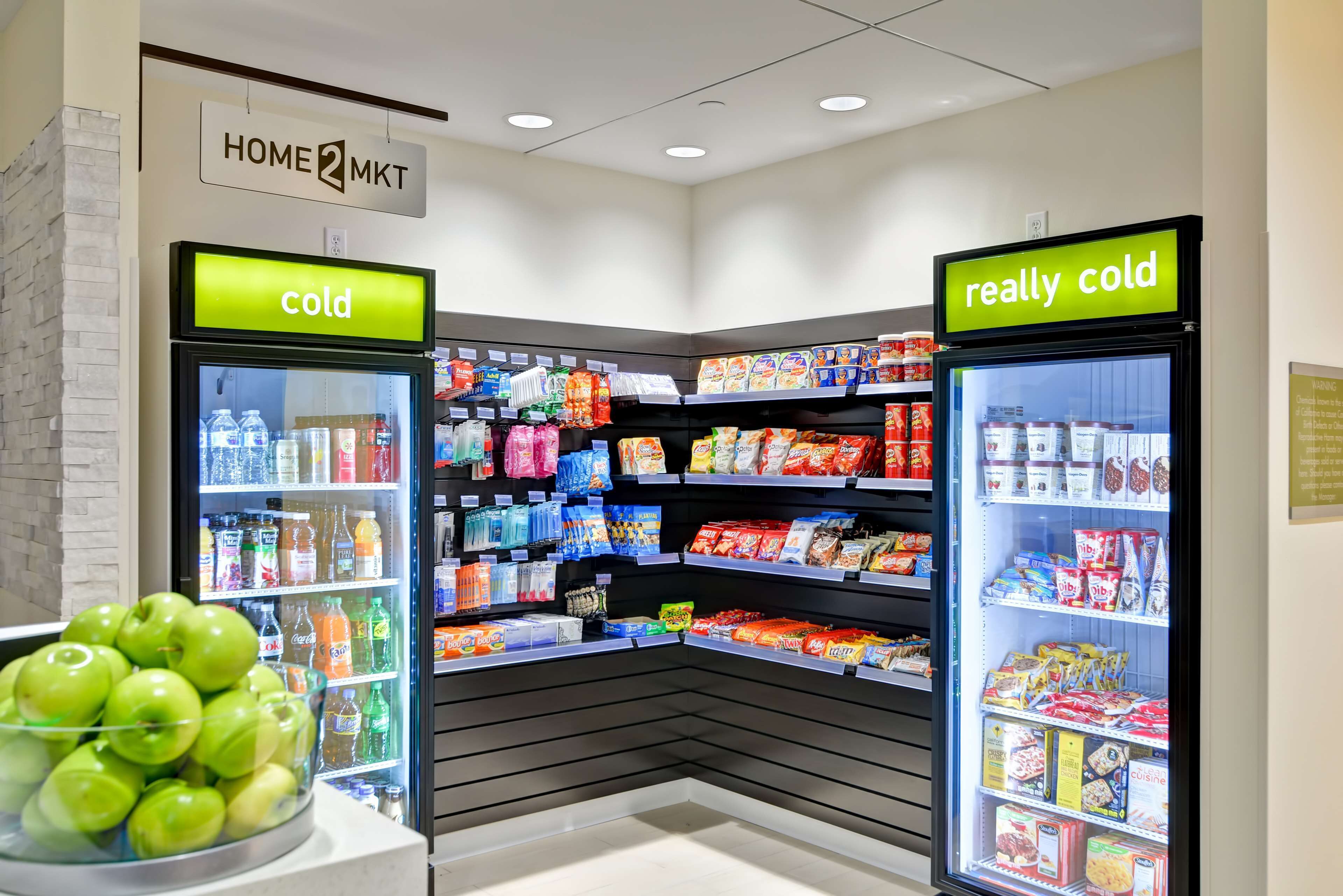 Una tienda de comestibles con dos vitrinas refrigeradas que indican 'frío' y 'muy frío', llena de diversas bebidas y aperitivos.