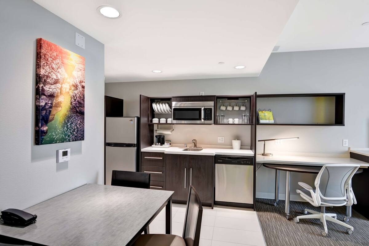 A modern kitchen with a microwave, stove, and dishwasher. There is a dining table with chairs and a small office area with a desk and chair.