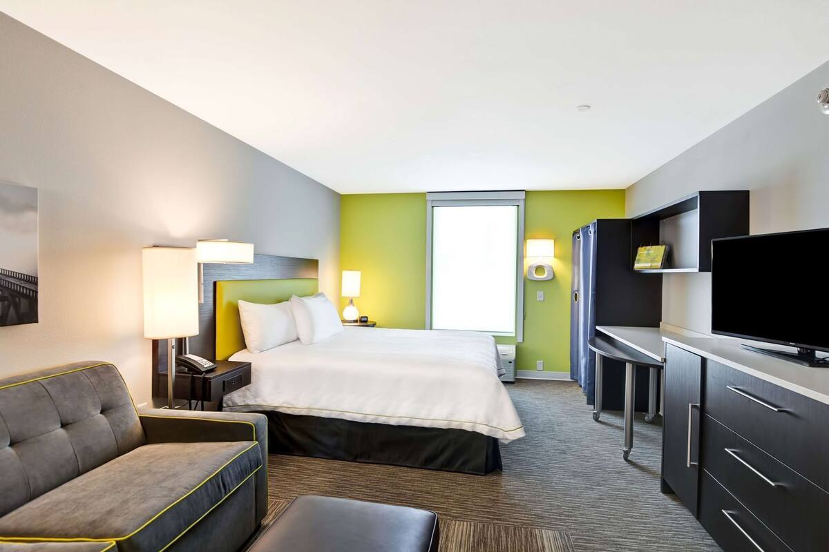 A hotel room with a bed, a desk, a TV, a sofa, and a lamp.