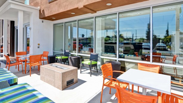 An outdoor seating area with tables and chairs, large windows, and a modern building facade. - Home2 Suites by Hilton Azusa (Azusa)