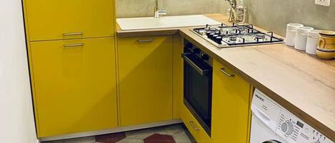 Una cocina compacta con armarios amarillos, horno empotrado, lavadora y suelo con diseño de baldosas hexagonales.