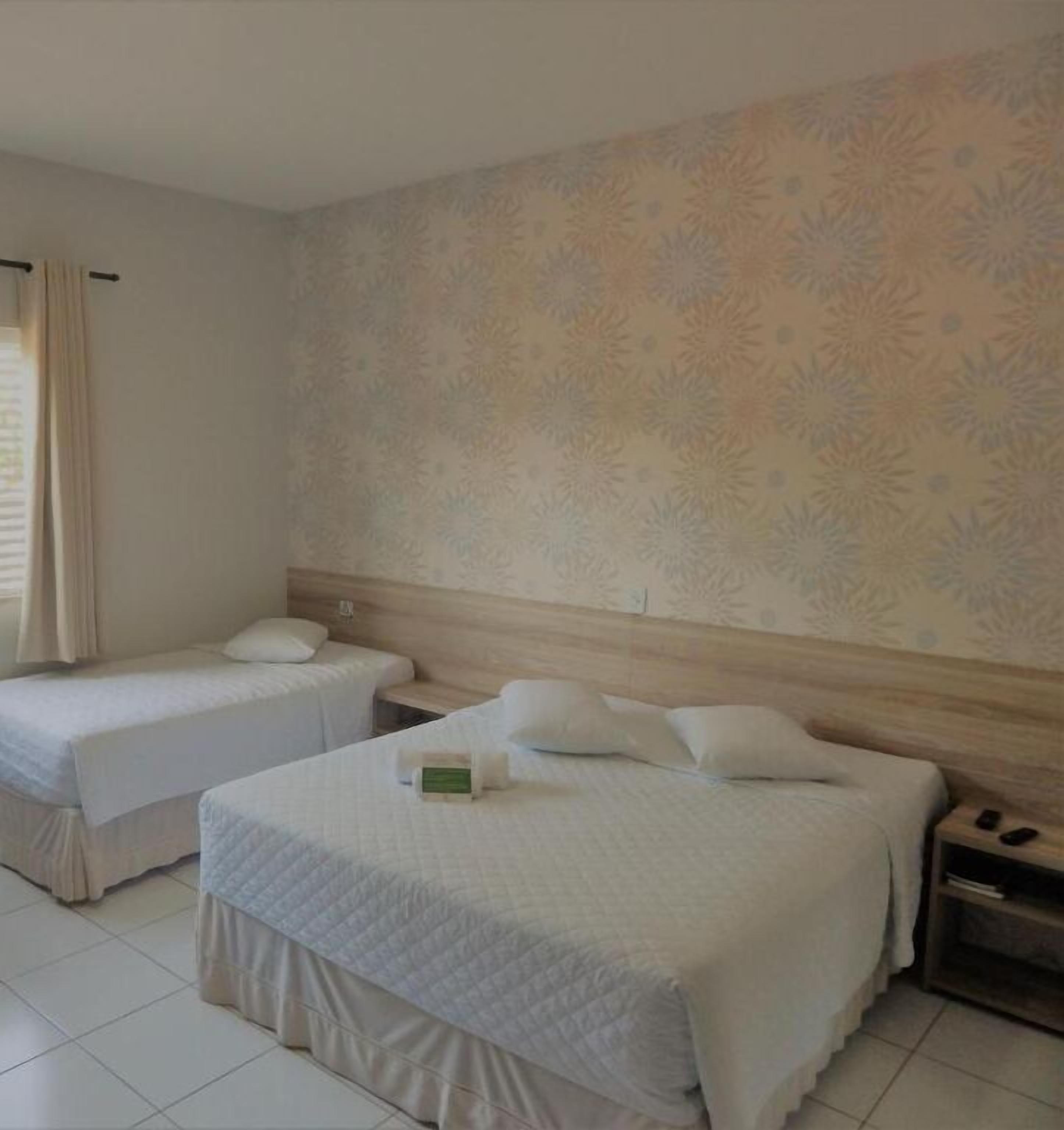 Habitación de hotel con dos camas individuales, cabecero de madera, mesita de noche y una pared con estampado floral.