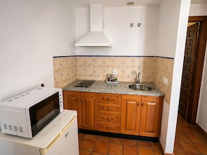 Una cocina compacta con armarios de madera, encimera de granito, microondas blanco y pileta de acero inoxidable.