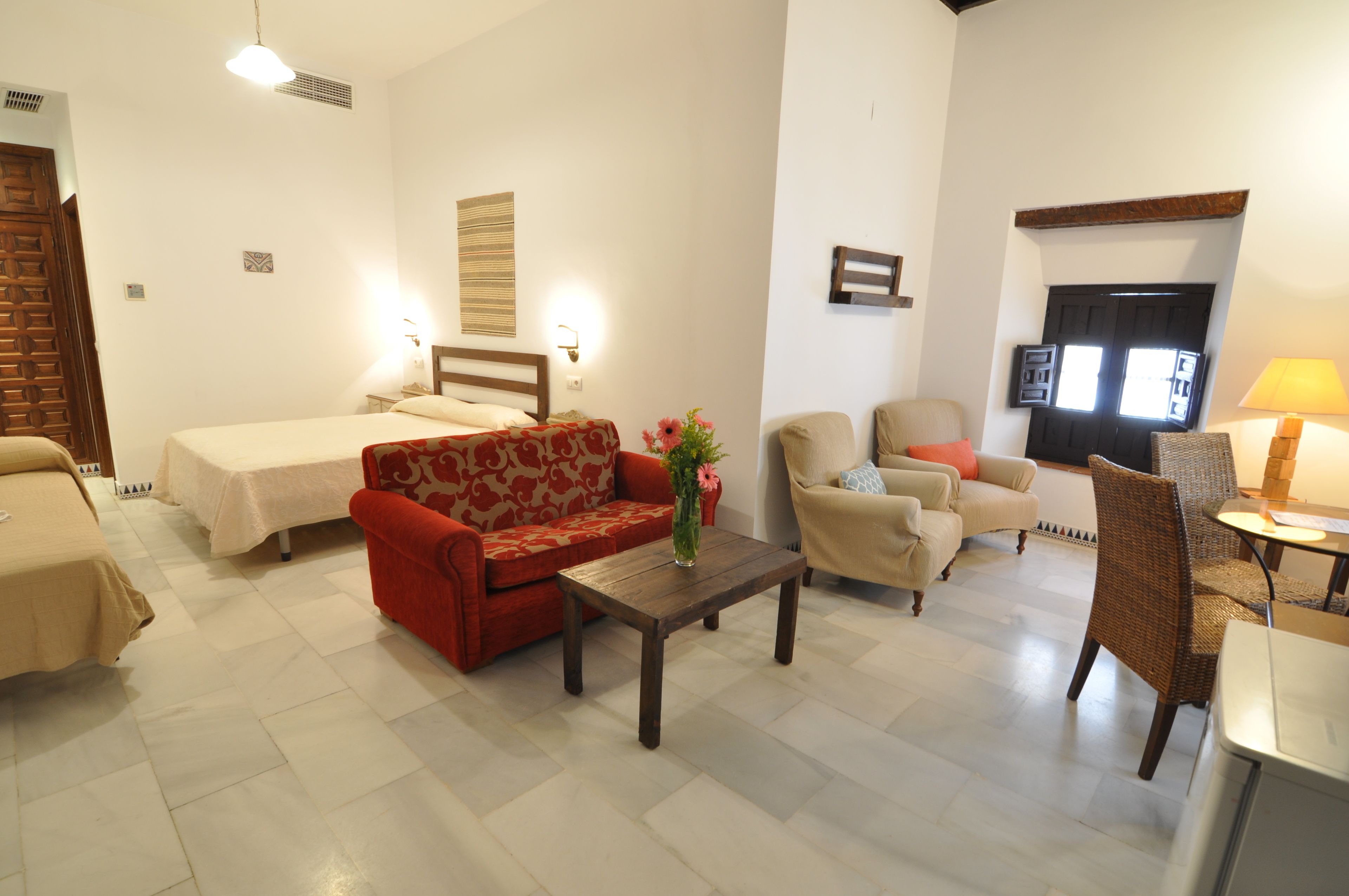 A hotel room with a bed, a red sofa, a wooden coffee table, and a chair.