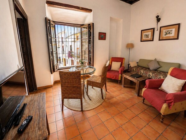 Una sala de estar con una mesa redonda, sillas de mimbre, un sillón rojo, un sofá y un mueble para televisor.