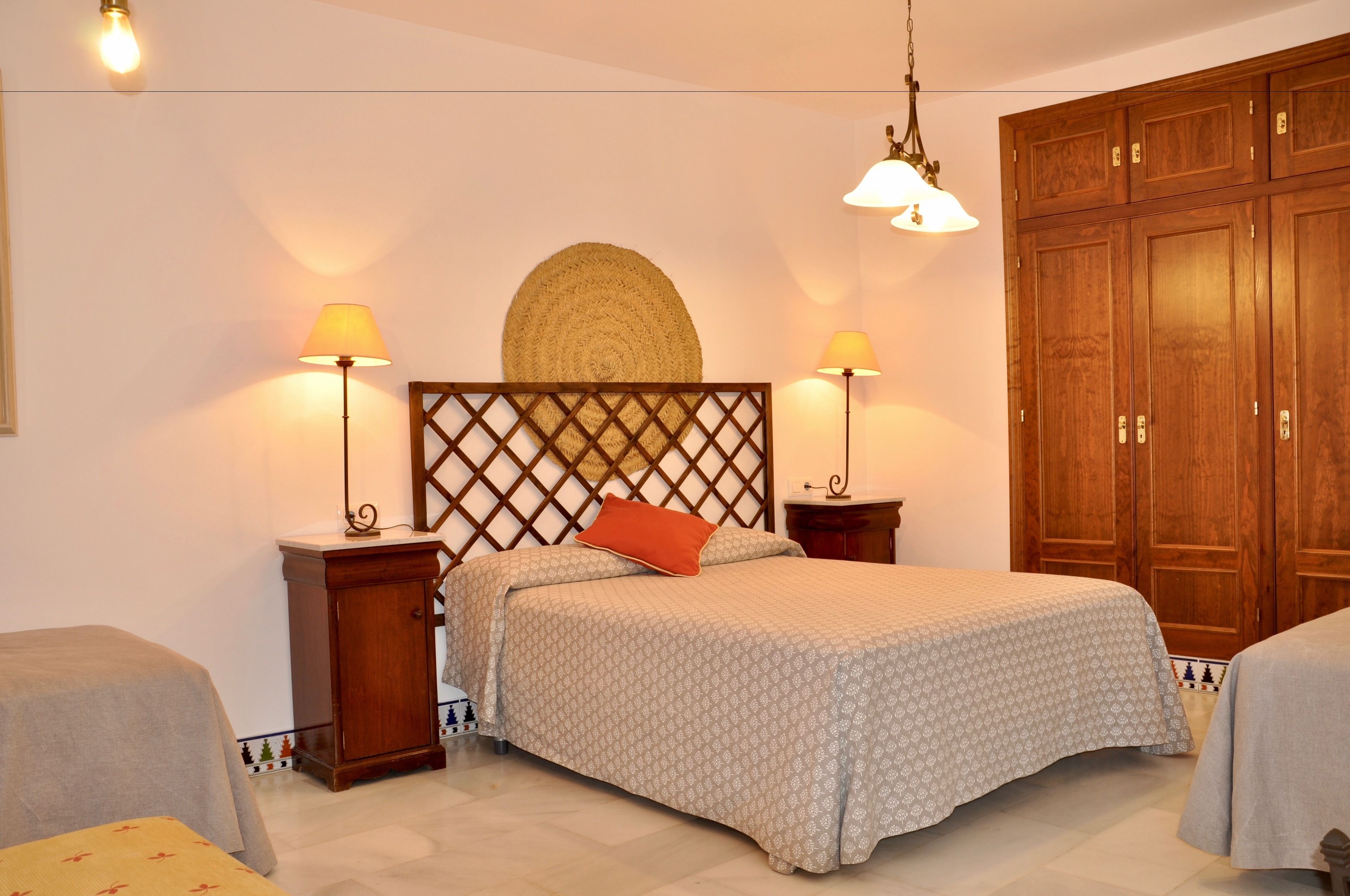 A neatly arranged bedroom with a bed, two bedside tables, a wooden wardrobe, and a decorative wall hanging.