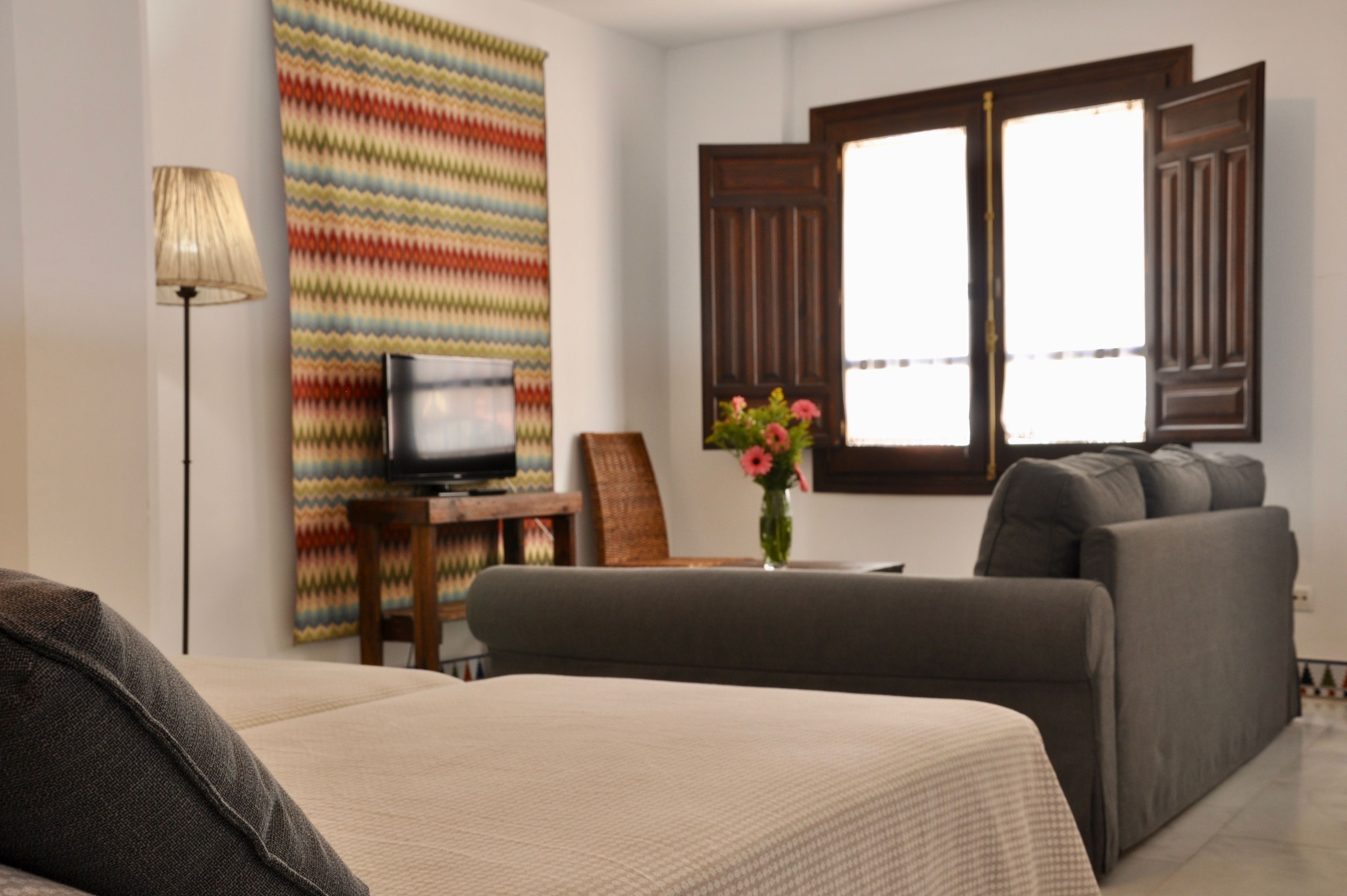 Una habitación de hotel con cama, sofá, televisión, lámpara y ventana con cortinas.