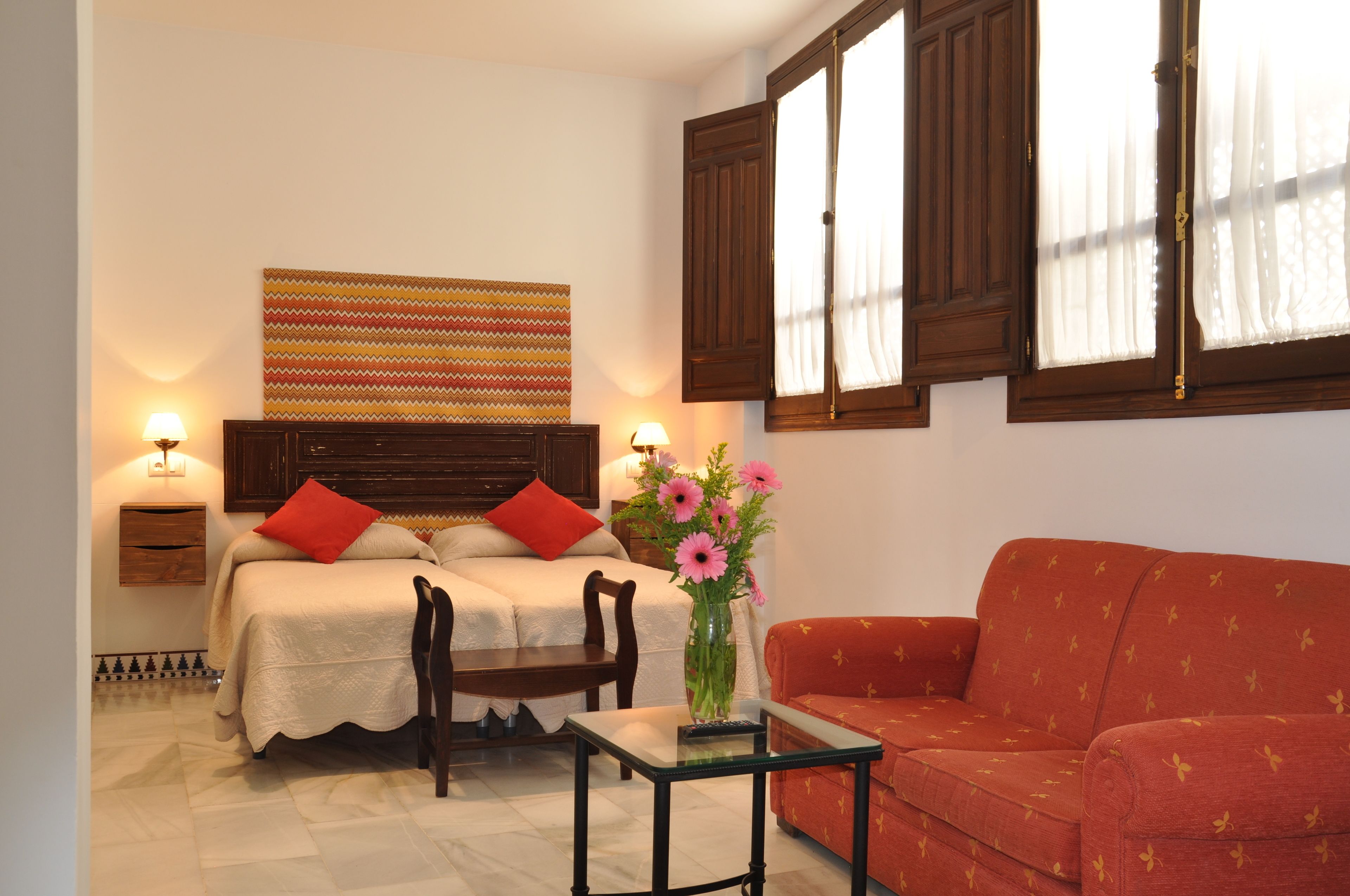 Un dormitorio con cama, dos mesitas de noche, un sillón y una ventana con cortinas.