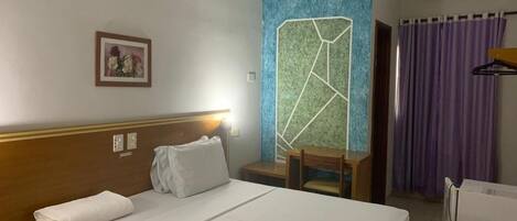 Habitación de hotel con cama, escritorio, silla, un cuadro en la pared y un aire acondicionado.