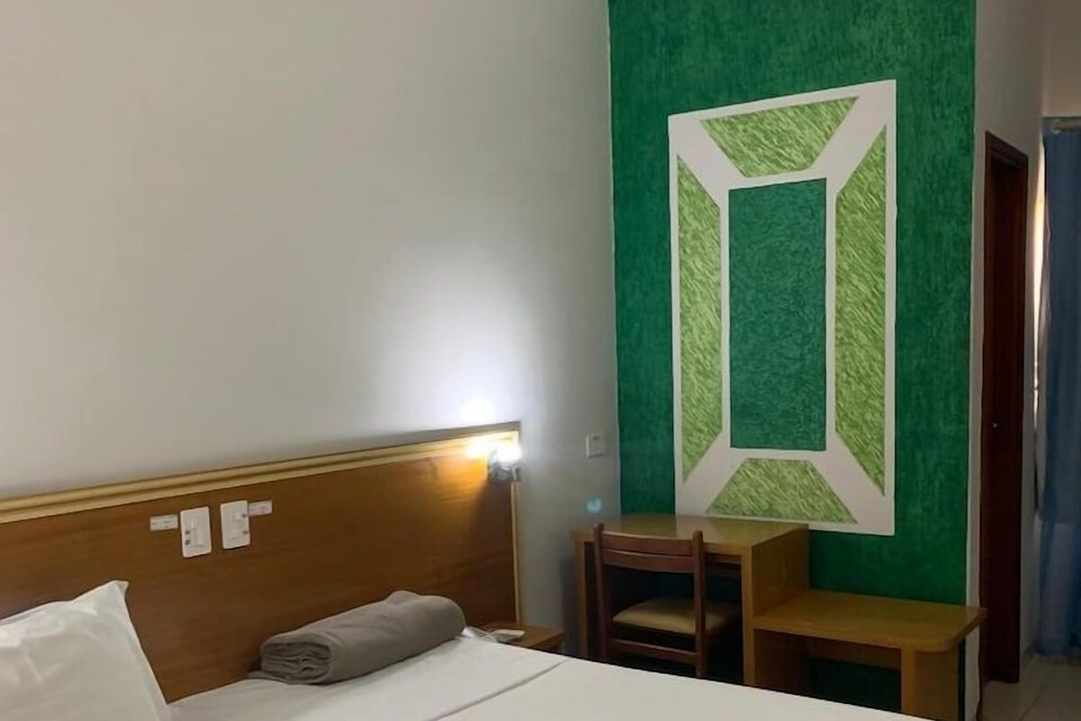 A hotel room with a bed, a desk, and a green accent wall.