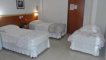 A hotel room with two single beds, a wooden headboard, a small table with a vase of flowers, and a door with a "No Smoking" sign.