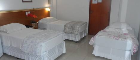 Habitación de hotel con dos camas individuales, cabecero de madera, una mesita con un florero y una puerta con un cartel de 'No Fumar'.