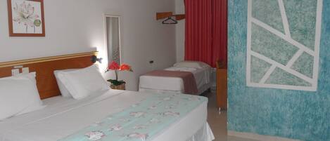 Una habitación de hotel con una cama grande, una cama más pequeña, un espejo, una cortina roja y una colcha con motivos florales.