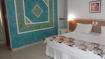 Quarto de hotel com uma cama, mesa de cabeceira, relógio de parede e um quadro na parede.