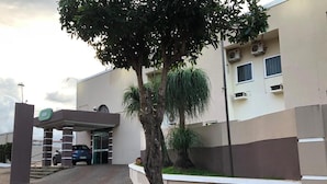 Entrada de un edificio con zona de estacionamiento techada, un árbol y un automóvil dentro.